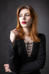 Red-haired gothic girl in a black dress on a gloomy background in the studio.