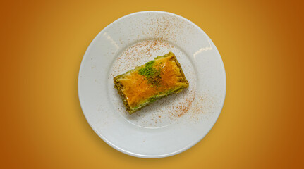 A single piece of baklava on a white plate against a warm orange background. Top view of a traditional Turkish dessert.