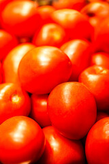 Close-up of vibrant red tomatoes piled together, showcasing their shiny, smooth surfaces and fresh, juicy appearance.