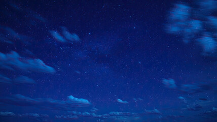Fototapeta premium Vast Star-Studded Night Sky with Deep Blue Hue, Bright and Luminous Stars Scattered Across, Soft Fluffy Clouds at the Bottom Adding Depth and Contrast, Creating a Serene and Enchanting Nighttime Atmos