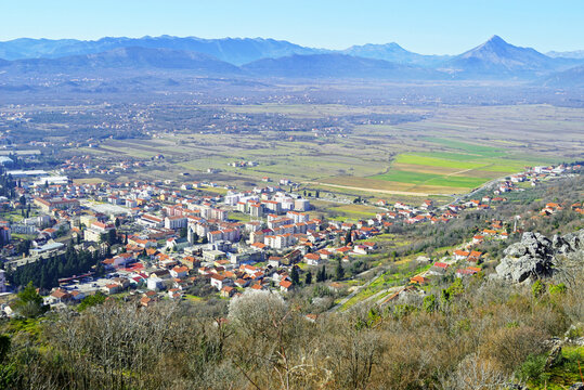 Ljubuski and its surroundings from Herceg Stjepan's Fortress. Aerial view of a small town in Bosnia and Herzegovina with low-rise buildings and a church surrounded by fields and mountains.