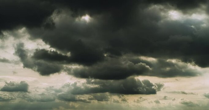 Timelapse of menacing dark grey clouds flying in the overcast sky and letting through some rays of sunlight creating strange underwater feeling to the scenery