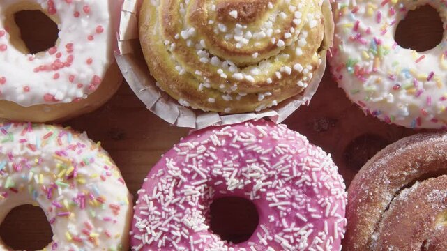 Overhead slider over tasty half-dozen donuts as hand chooses pink one
