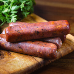 pile of raw red beef smoke sausage with collagen casing on top of wooden cutting board, with spice on the background