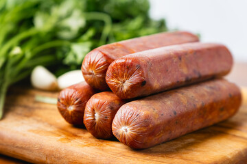 pile of raw red beef smoke sausage with collagen casing on top of wooden cutting board, with spice on the background