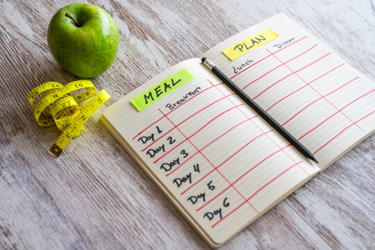 Organized Meal Planning Notebook With Daily Menu For Health, Fitness, And Nutrition Featuring A Green Apple And Written Planner.Concept Of Maintaining And Improving Health.Healthy Meal Or Menu.