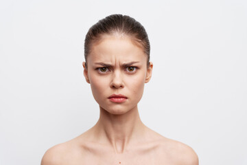 Serious woman with a neutral expression, bare shoulders, clear skin, and a focused gaze on a plain...