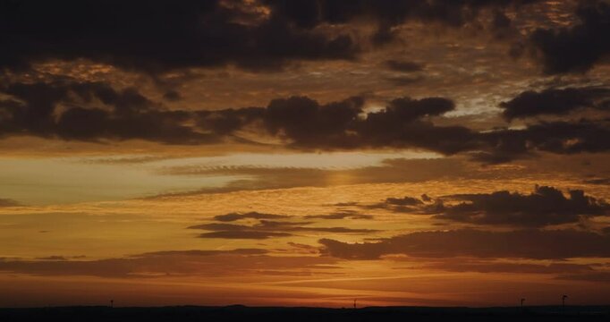 Timelapse of beautiful orange sunset sky with faster moving lower layer of contrasting dark clouds and brightly illuminated colorful higher layer of clouds moving slower