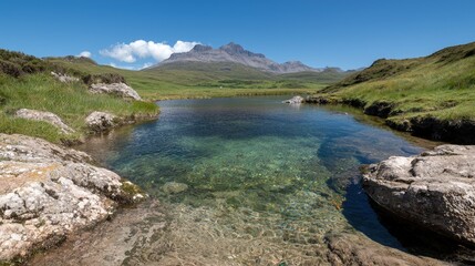 Crystal clear mountain lake with visible bottom, rocks, and a majestic peak in the background under a blue sky.
