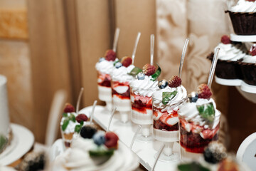 desserts in transparent cups that stand on a tray. Each cup is filled with layers of whipped cream and berries such as raspberries and blueberries.