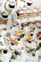 cupcakes placed on a white stand. The cupcakes are decorated with white frosting and a variety of berries such as blackberries and raspberries, as well as fruit pieces and green leaves.