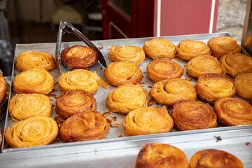 Des pâtisseries Kouign-Amann fraîchement cuites déposer dans un présentoir de commerce qui vend dans la rue. Grande quantité avec une pince en métal pour le service.
