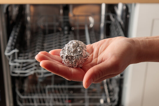 A woman puts a ball of aluminum foil into the dishwasher, cost-effective, environmentally friendly, and highly effective hack, the secret to sparkling silverware, spotless glassware and cutlery