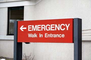 Naklejka premium A red sign with white text reads EMERGENCY Walk In Entrance with an arrow pointing left.
