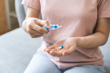 Sick ill asian young woman, girl hand taking tablet pill capsule out from blister pack, painkiller medicine from stomach pain, head ache, pain for treatment, take drug or vitamin at home, health care.
