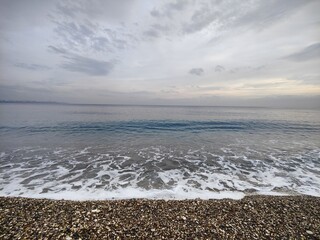 The Silent Shore: A Metaphor of Endless Horizons and Fleeting Waves, Where Pebbled Stillness Meets the Moody Sky, Reflecting a Timeless Serenity Amid the Calm Before the Storm in Nature’s Unspoken.