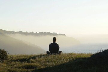 A person sits on the top of a lush green hillside, enjoying the view