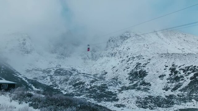 Aerial view of Iconic Red cable car on the way from Lomnick&yacute; &Scaron;t&iacute;t to Skalnat&eacute; pleso in winter (4K).
