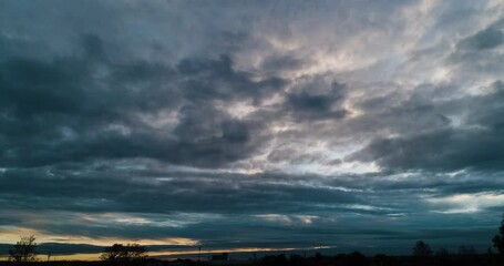 Timelapse of the overcast sky with dark storm clouds moving toward camera and orange glow of sunset on the horizon