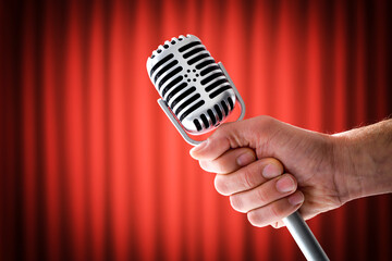 Hand holding vintage microphone on stage with red curtains background