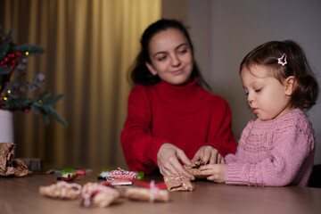 Fototapeta premium mother and her little child girl together wrapping Christmas gifts at home in the evening, preparing presents for family.