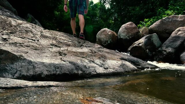 A tourist crosses a stream and climbs over rocks in the jungle