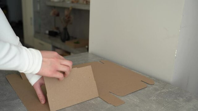 Female hands assembling a kraft cardboard foldable box on a table