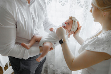 A man and a woman are holding a baby. The baby is wearing a white hat and a pacifier. The scene is warm and loving, with the family bonding over the new addition to their family