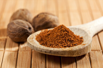 Ground nutmeg on wooden spoon closeup, whole nutmeg in background