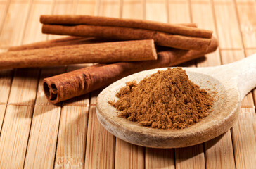 Ground cinnamon on wooden spoon, cinnamon sticks in background