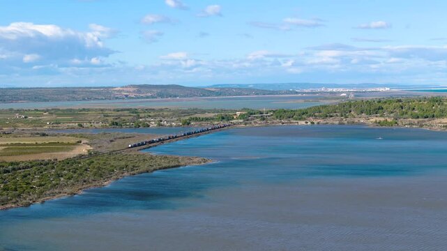 Aerial view of a train crossing tranquil waters near Narbonne, France. A scenic route highlighting international connections, tourism, and freight transport in a coastal landscape.