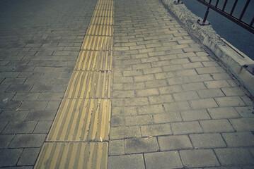 Uneven paving slabs with dents and surface defects on sidewalk, risks to pedestrian safety and the need for urban infrastructure repair. Tactile tile and hazards for visually impaired pedestrians