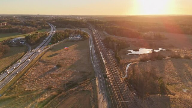 Rail tracks and a motorway at sunset, high speed train passing by, cars on the motorway. E4 between Stockholm and Arlanda airport.
