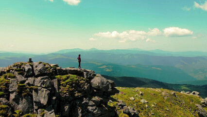 Woman standing on rocky mountain peak overlooking vast landscapes. A lone woman stands atop a rocky...