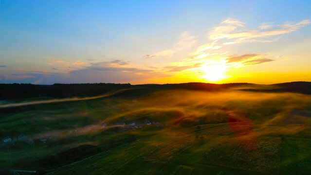 Sunrise over misty countryside landscape with golden light. A stunning aerial view of a countryside landscape at sunrise, with golden light streaming through a soft layer of mist.