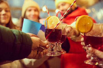 Close-up of glasses of mulled wine with orange slices and striped straws. Group of friends gathering outdoors, celebrating winter holidays. Concept of winter holidays, Christmas, traditions
