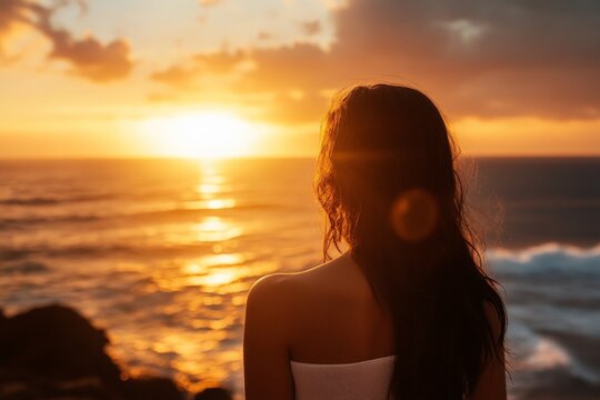 A woman stands gazing at a breathtaking sunset over the ocean, capturing the essence of peace, solitude, and introspection in golden evening light reflections.