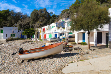 Barcas varadas frente a casitas coloridas junto a playa de cantos rodados en Cala S'Alger.