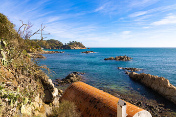 Vista costera con caseta varadero, rocas y mar azul en Cala S'Alger, Costa Brava.