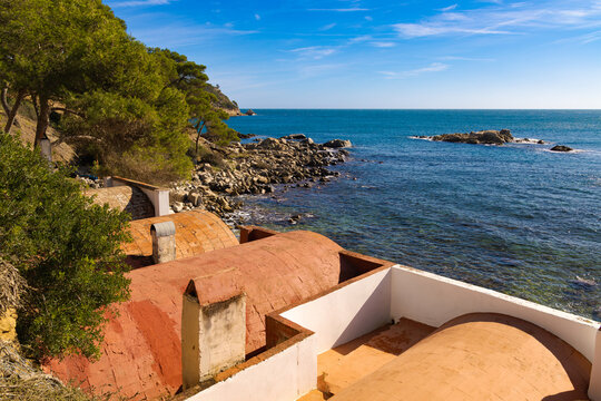 Casetas varadero con techos curvos junto a la costa rocosa y mar cristalino en Cala S'Alger.