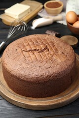 Tasty chocolate sponge cake and ingredients on black wooden table, closeup