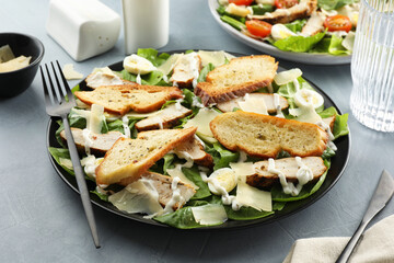 Delicious Caesar salad with chicken on grey textured table