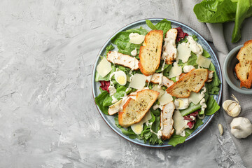 Tasty Caesar salad with chicken and ingredients on gray textured table, flat lay. Space for text