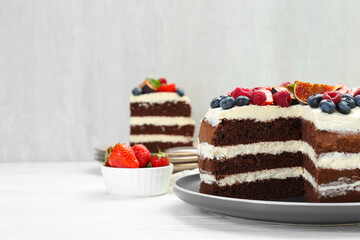 Delicious chocolate sponge cake with berries served on white wooden table, closeup