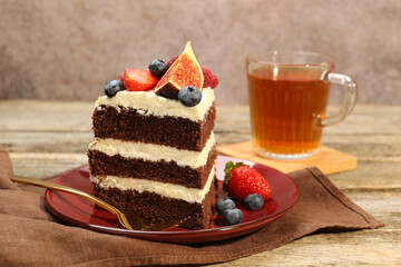 Piece of delicious chocolate sponge cake with berries and tea on wooden table, closeup