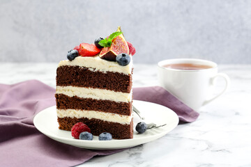 Piece of delicious chocolate sponge cake with berries and tea on white table, closeup
