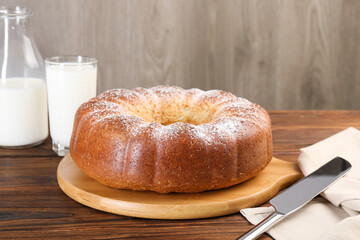 Freshly baked sponge cake, knife and milk on wooden table, closeup