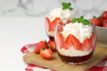 Tasty trifle dessert. Sponge cake, strawberries, jam and whipped cream in glasses on white table, closeup