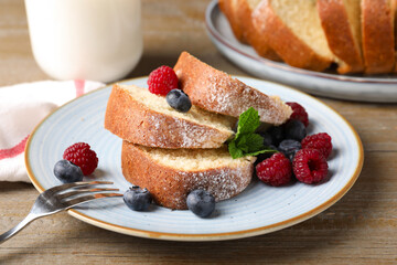 Pieces of freshly baked sponge cake, berries and milk on wooden table, closeup