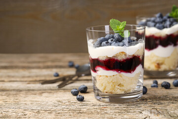 Tasty trifle dessert. Sponge cake, blueberries, jam and whipped cream in glasses on wooden table, closeup. Space for text